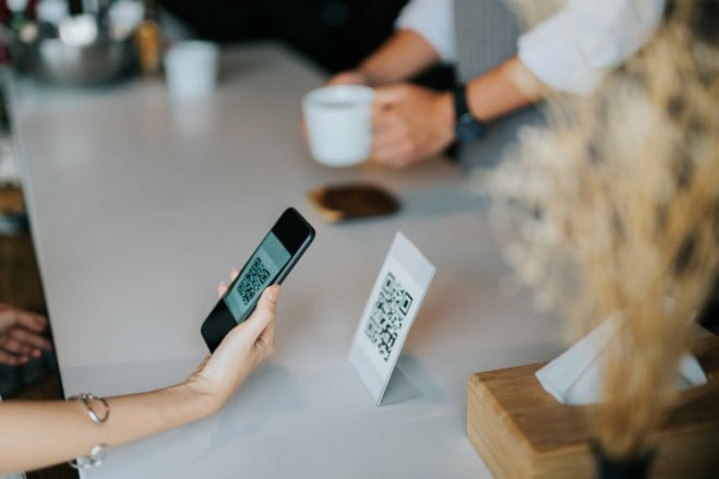Kvinnehånd holder mobiltelefon foran en QR-kode på kafe