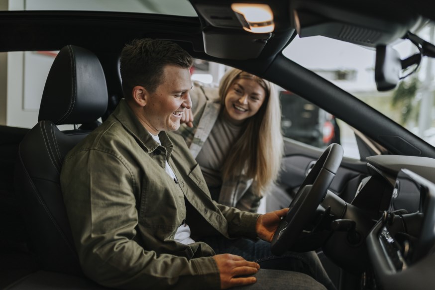 Smilende mann sitter i bil og glad ung jente står utenfor